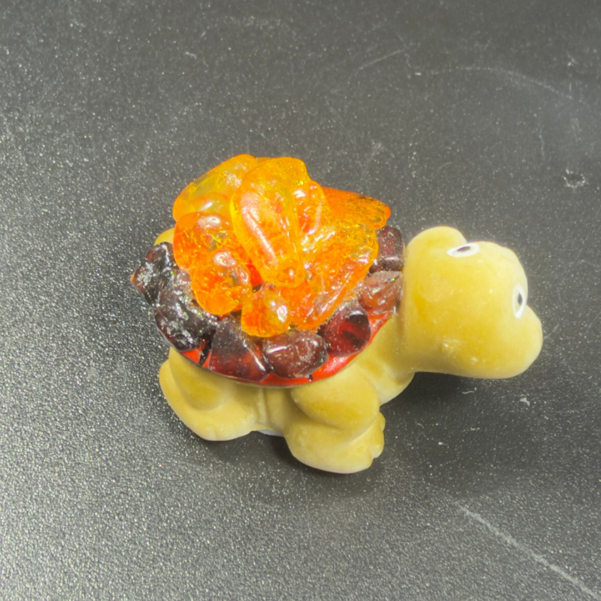 Close-up of the KIZIMA® mini turtle: cream ceramic body, golden-orange and cognac Baltic amber shell