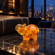 KIZIMA miniature Baltic amber elephant with raised trunk beside a leather-bound book on black marble, with Manhattan lights in the background.