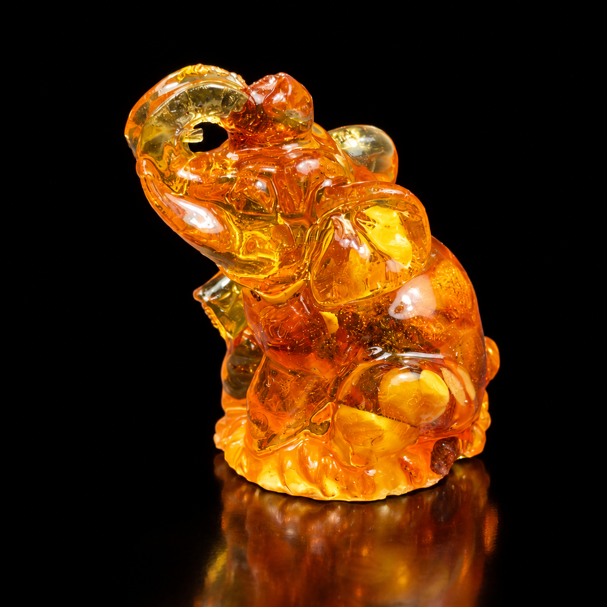 Made in USA Natural Baltic Amber seated elephant figurine, 6 cm, trunk raised, honey-cognac amber, black studio background — KIZIMA®