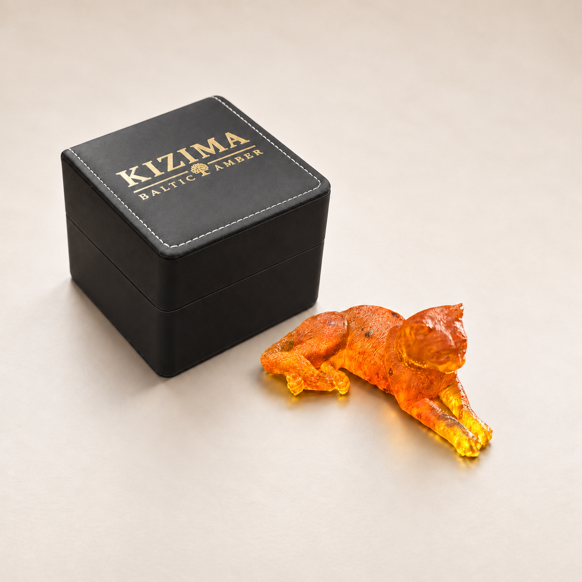 Made in USA Natural Baltic Amber reclining cat figurine by KIZIMA® beside its black branded KIZIMA® gift box at true scale