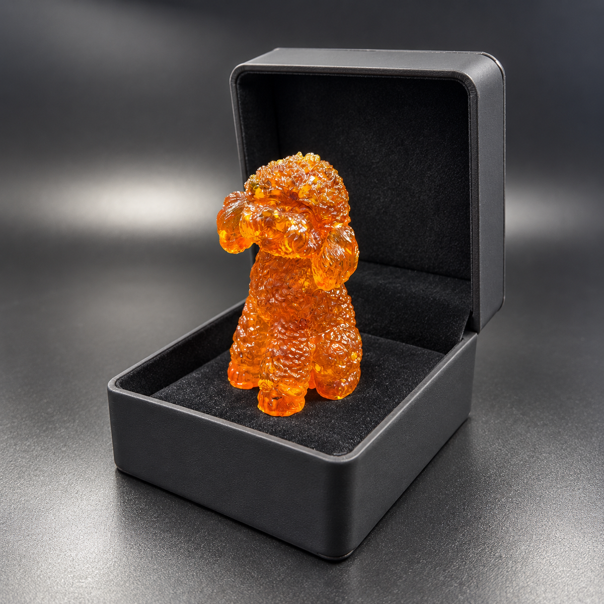 Curly-coated amber poodle displayed upright in an open charcoal gift box, with its paws on the black lining and the lid raised behind it.