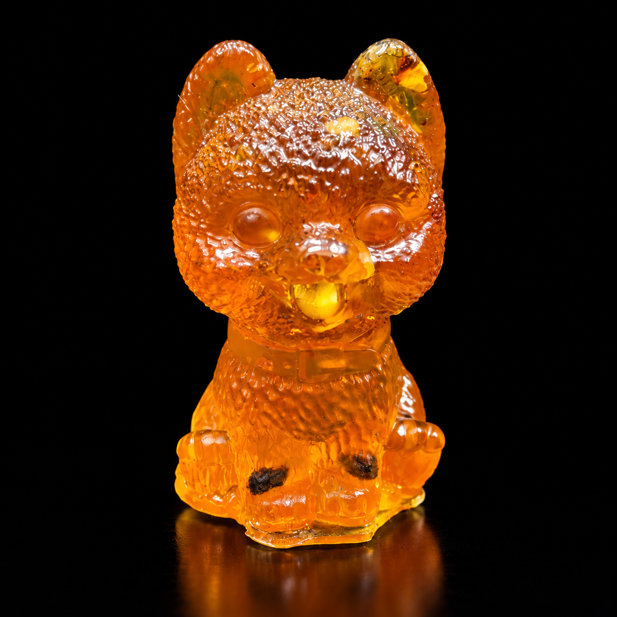 Front view of an amber fluffy puppy with upright rounded ears, a textured head, collar and tongue showing, on reflective black.