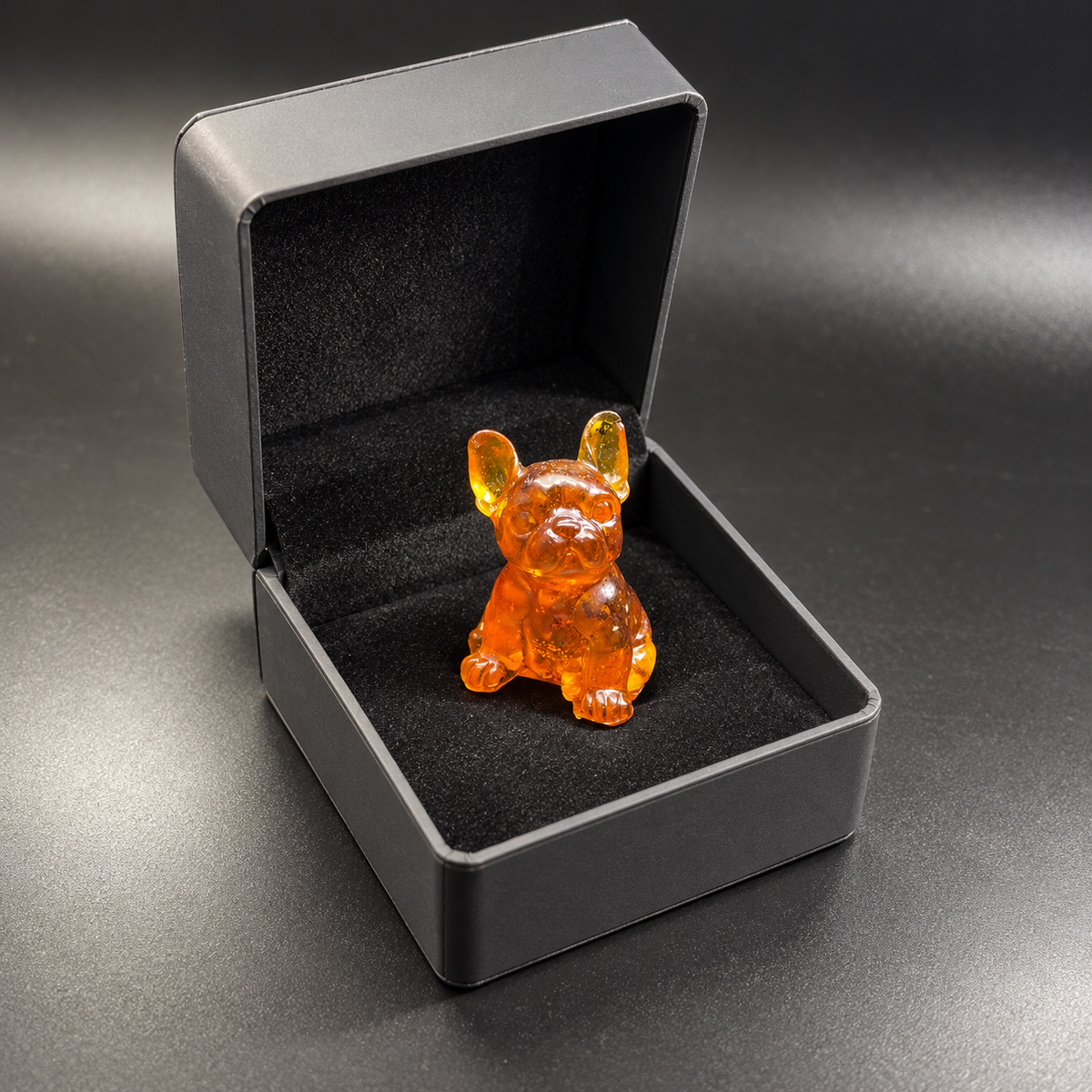Amber French Bulldog with tall bat ears displayed upright in the black-lined base of an open charcoal hinged gift box.