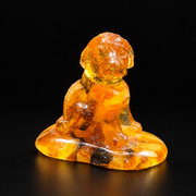 Amber puppy seated on a broad oval base, with hanging ears, small front paws and dark inclusions, against a black background.