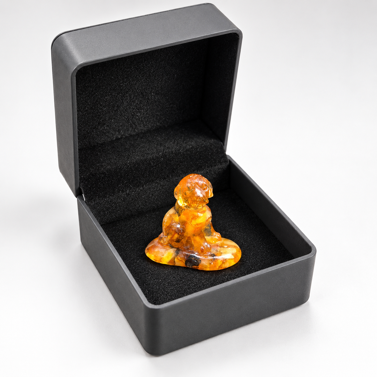 Amber puppy and its oval base displayed in an open charcoal gift box on white, with black lining around the miniature.