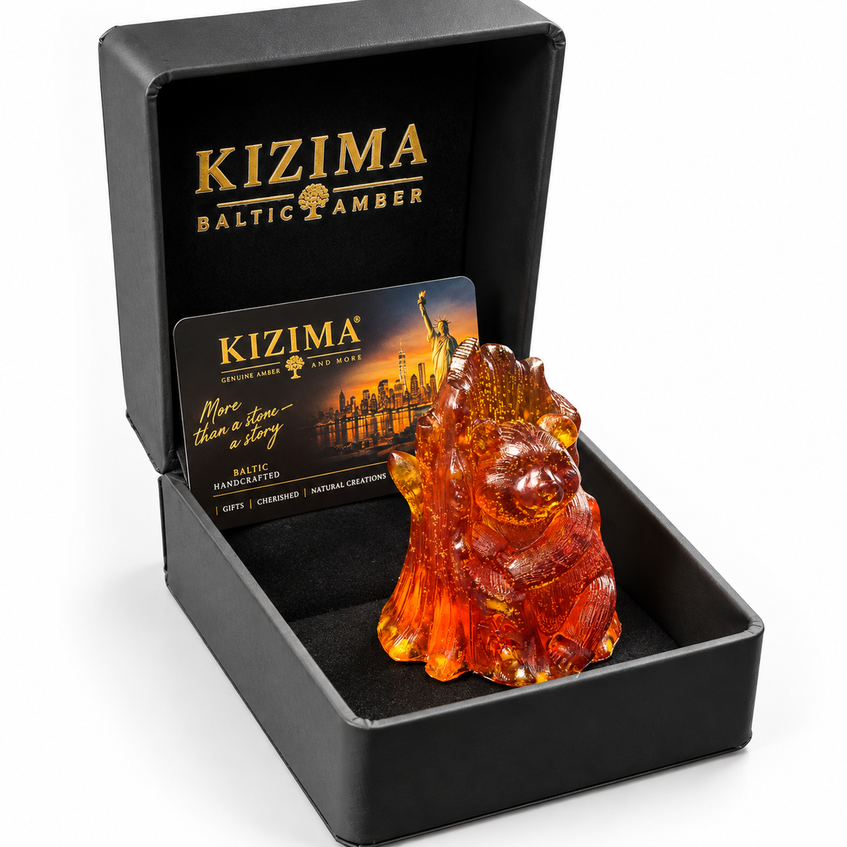 Cognac amber bear hugging a tree trunk inside an open black KIZIMA gift box with a branded card on a white background.