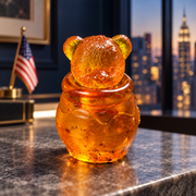 Golden bear head honey jar on a gray stone console, with an American flag and Manhattan buildings softly blurred behind it.