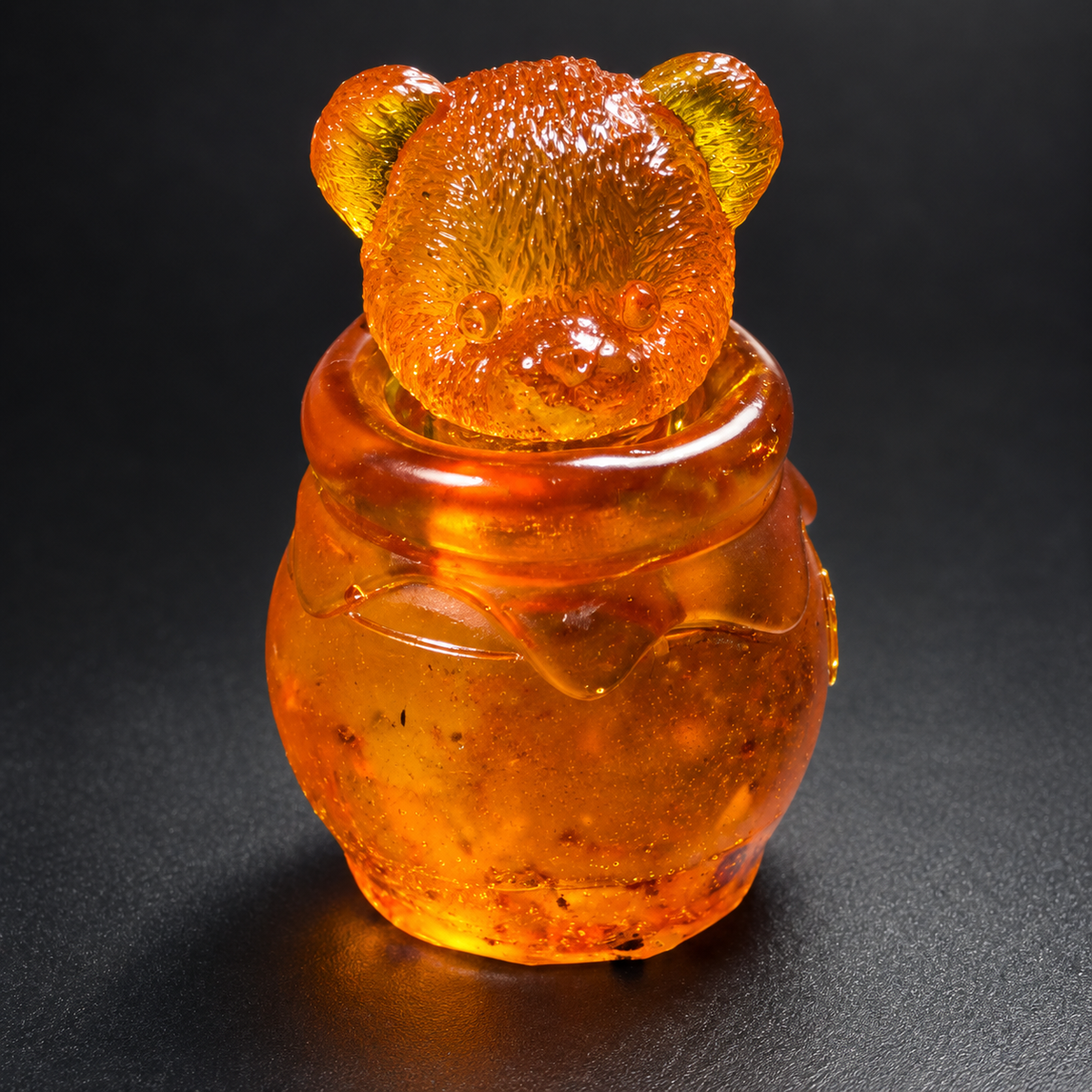 Golden amber honey jar with a textured bear head lid, illuminated on a charcoal studio background.