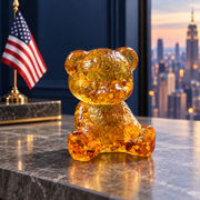 Golden amber teddy bear on a stone console beside an American desk flag, with navy walls and the Manhattan skyline in the background.