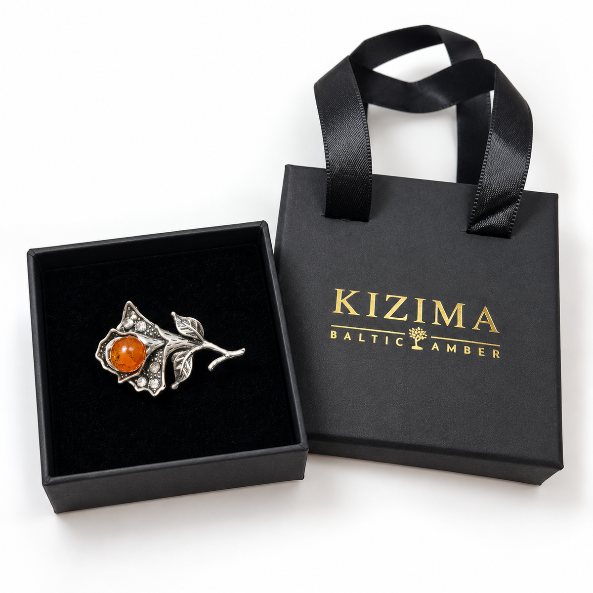 KIZIMA silver-tone flower brooch 20N0120q3.9 with orange amber and clear crystals in a black KIZIMA gift box beside the matching bag.