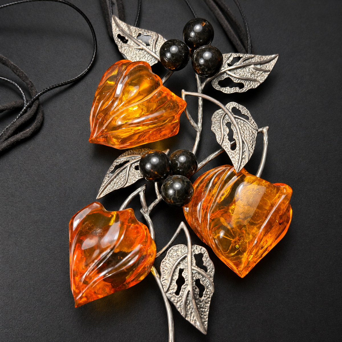 Close-up of three carved amber buds, six dark beads and pierced metal leaves, studio view 3