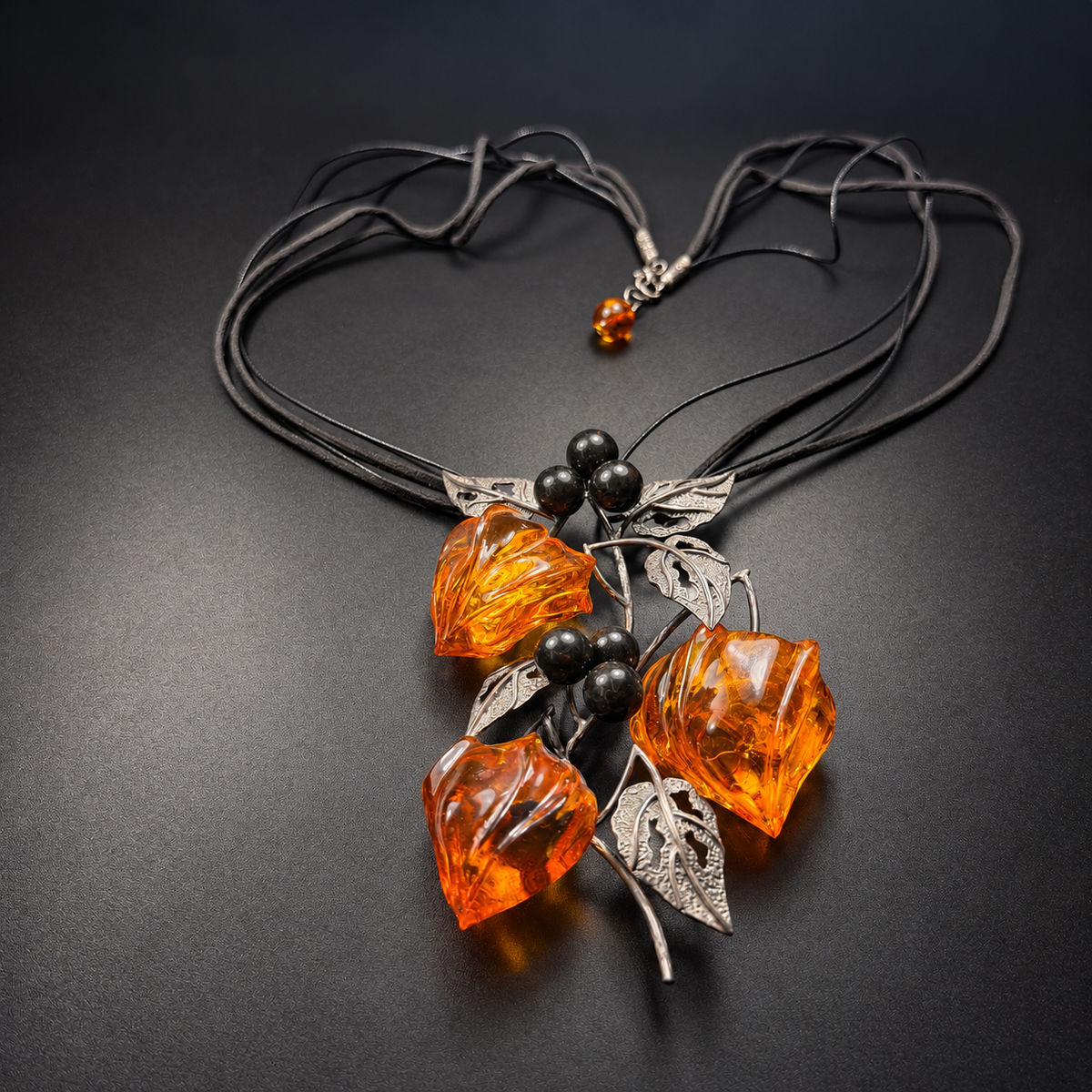Front layout of three-bud amber necklace with black cords and leaf pendant, studio view 10
