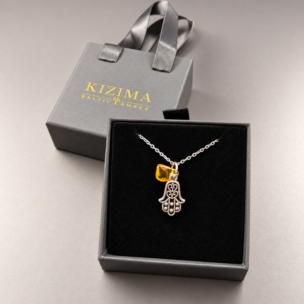 Made in USA Natural Baltic Amber Hamsa necklace by KIZIMA® in its gray gift box with matching ribbon-handle gift bag