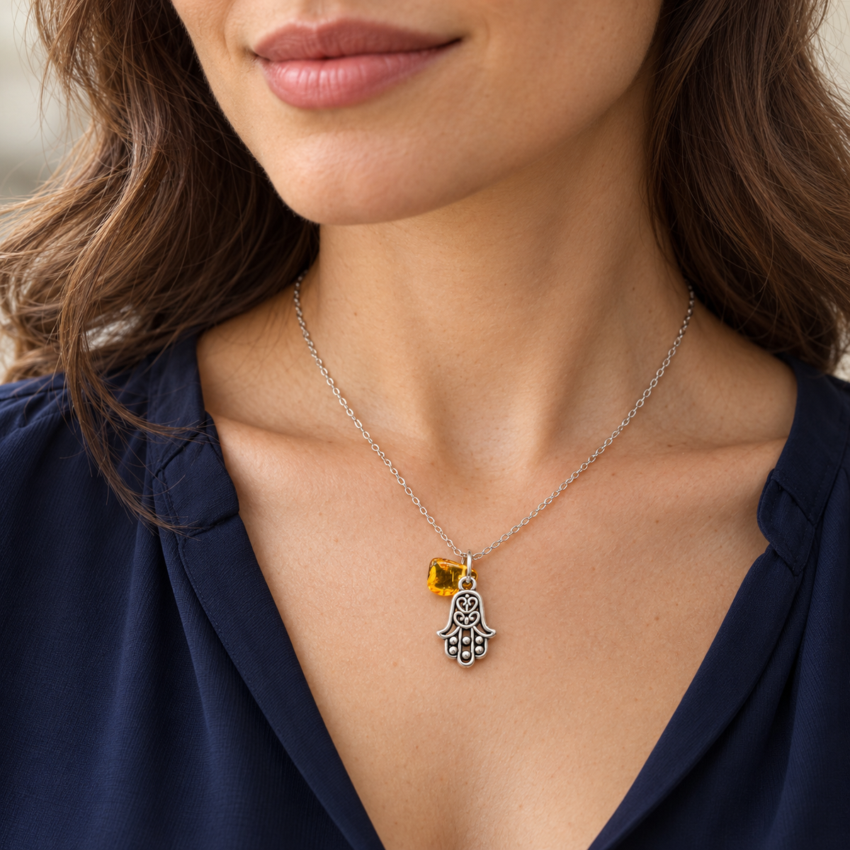Woman in a navy blouse wearing the Made in USA Natural Baltic Amber Hamsa pendant necklace by KIZIMA® on its 45 cm chain