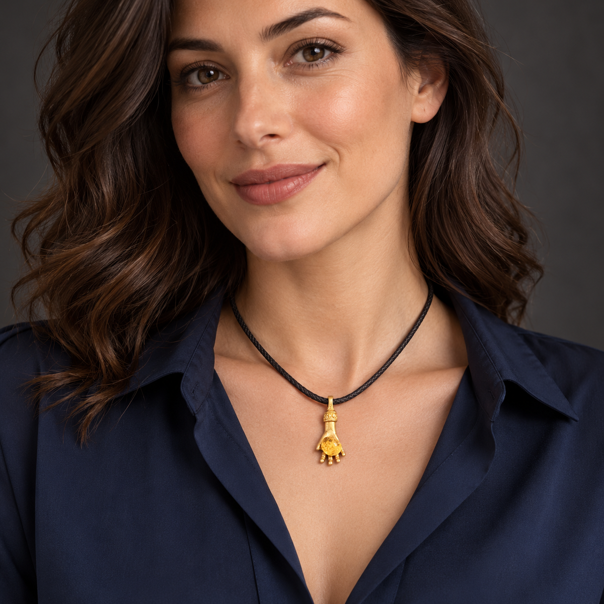 Adult woman in a navy blouse wearing the KIZIMA money hand pendant with natural Baltic amber, approximately 3 cm tall, on a 40 cm dark cord.