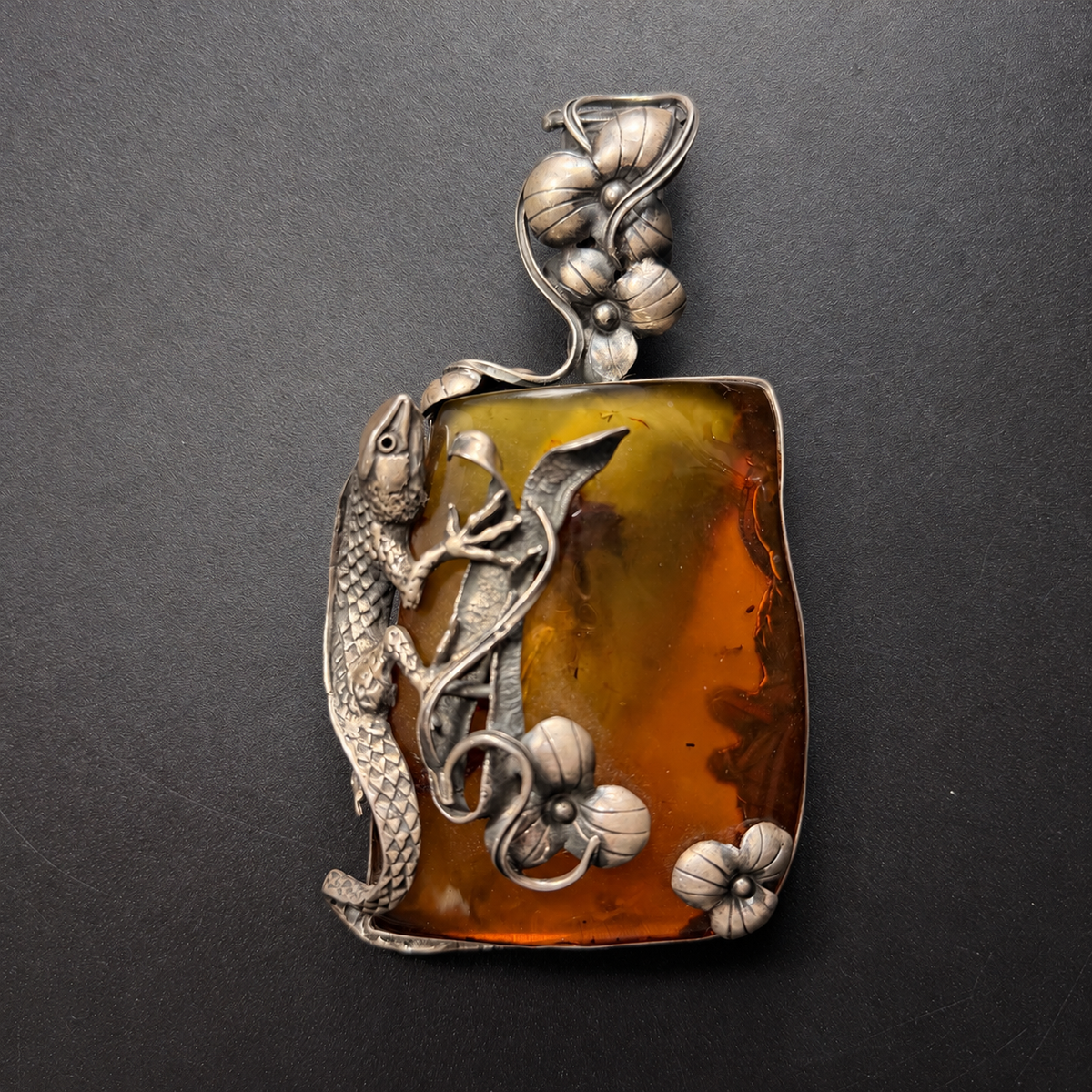 Near-frontal view of the large amber lizard pendant with floral details at the bail and lower corners.