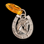 KIZIMA horseshoe and horse head amulet with golden Baltic amber, silver-tone metal detail on a black studio background
