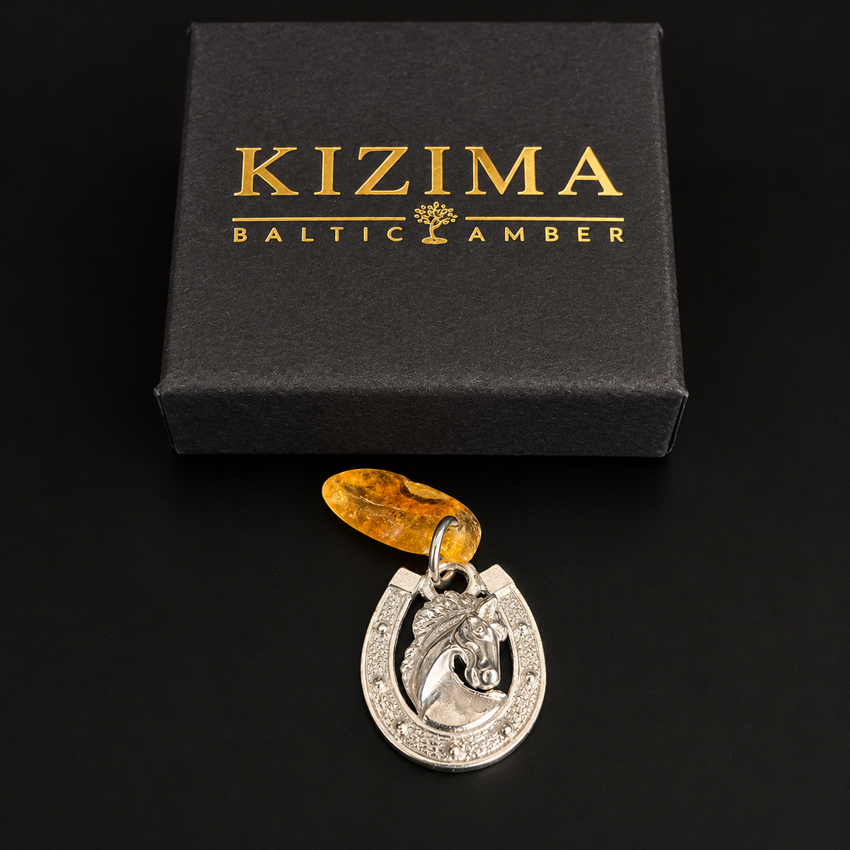 KIZIMA horseshoe and horse head amber amulet beside its black gift box with gold KIZIMA Baltic Amber lettering