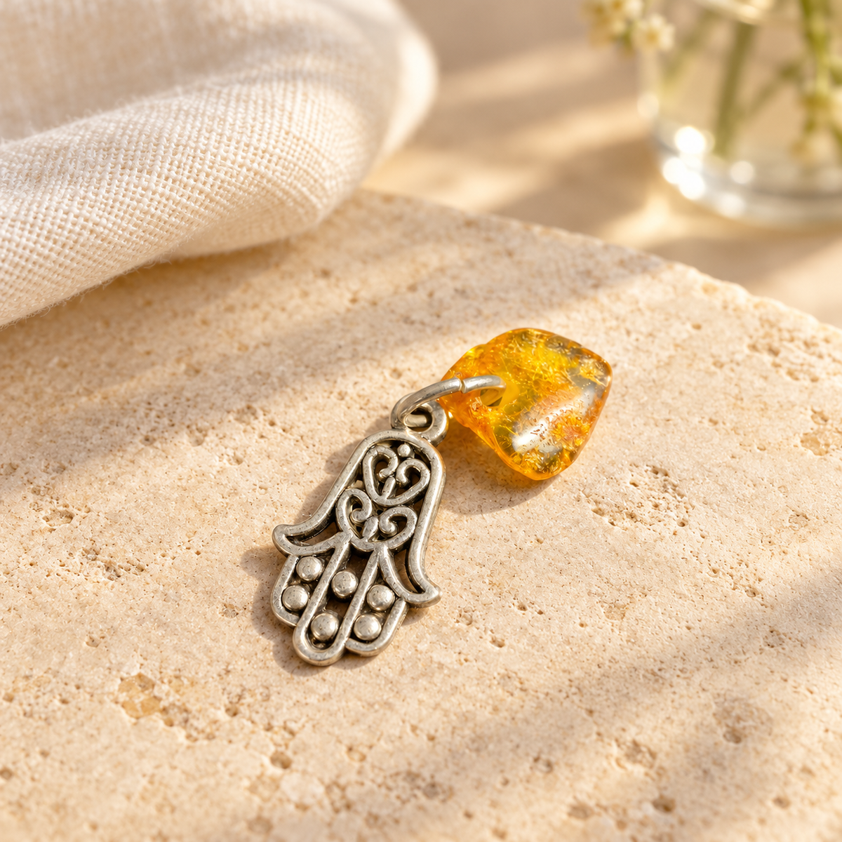 Made in USA Natural Baltic Amber Hamsa amulet by KIZIMA® on a pale stone tabletop beside folded linen