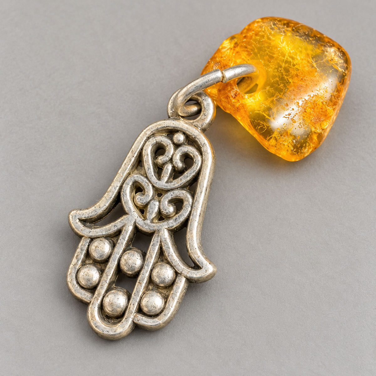 Close-up of the Made in USA Natural Baltic Amber Hamsa amulet by KIZIMA® showing inclusions in the golden amber and the metal rings