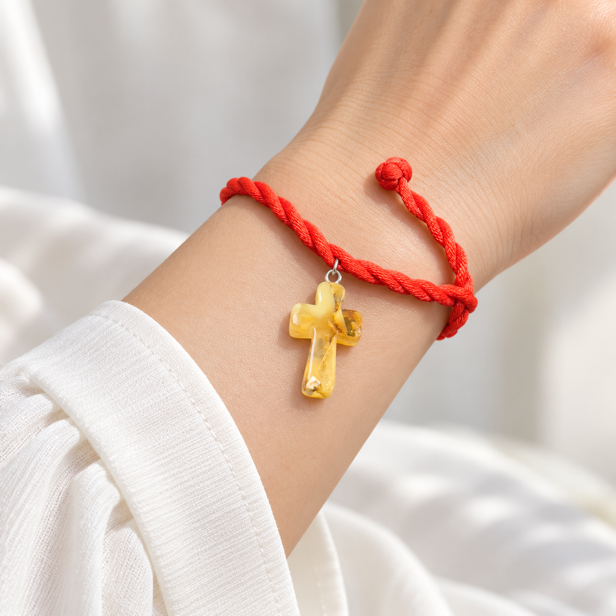 KIZIMA yellow amber cross pendant on red twisted rope bracelet on a young adult woman's wrist
