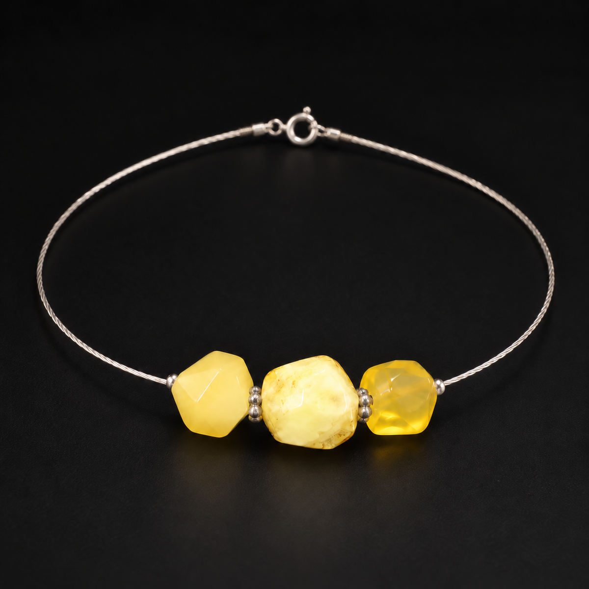 KIZIMA three-stone yellow amber bracelet with a thin silver-colored cable, photographed under soft studio light on black.
