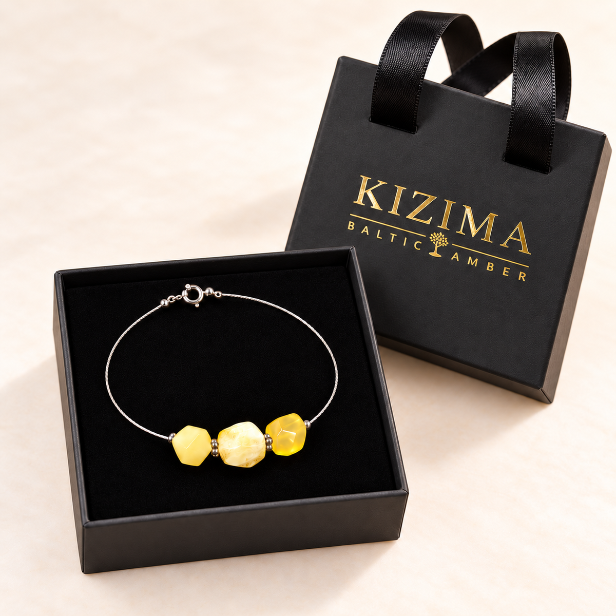 Three-stone yellow amber cable bracelet in an open black KIZIMA velvet-lined gift box, beside its handled lid with gold logo.