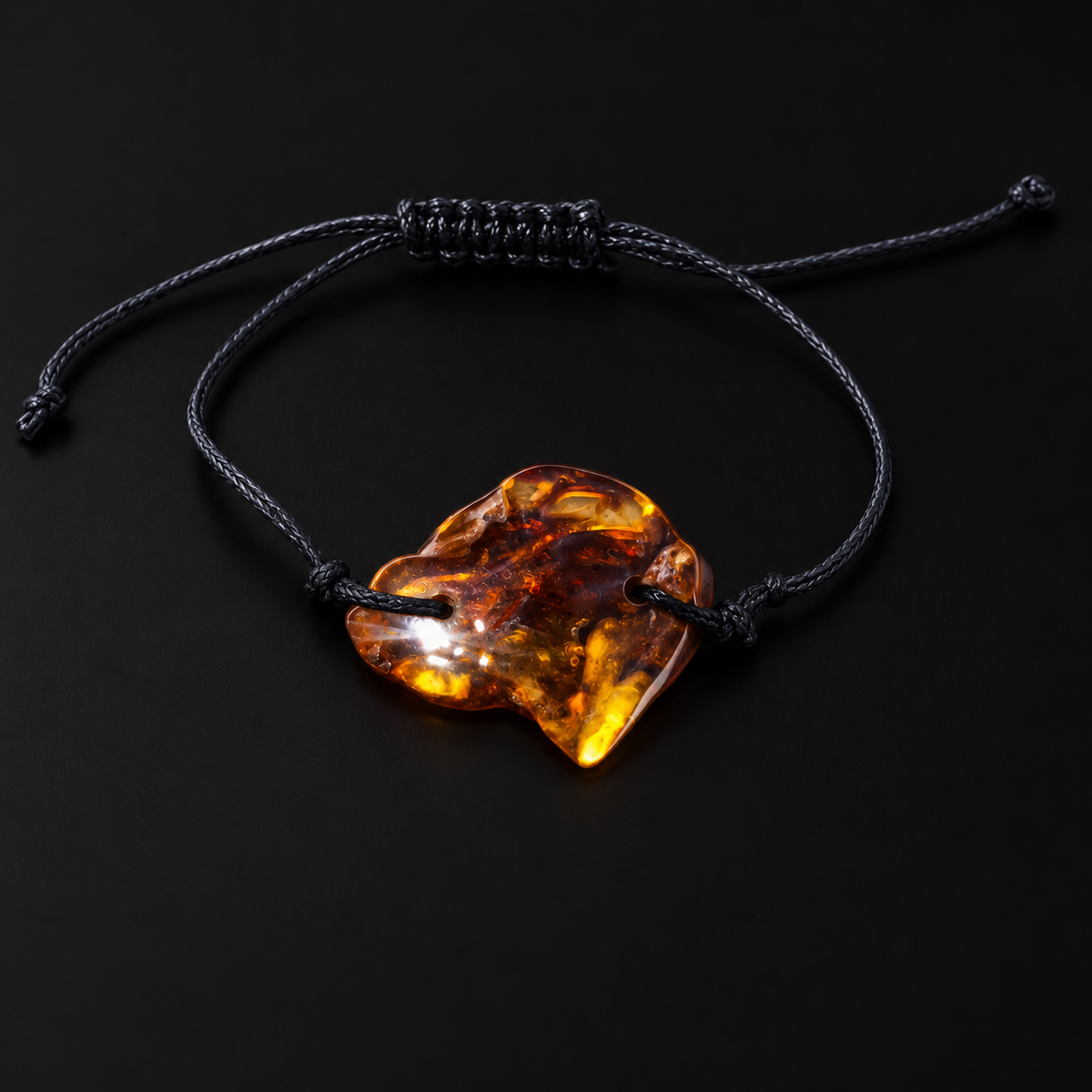 KIZIMA 3G0100q2.32 asymmetrical cognac amber slab bracelet and black cord on a dark studio surface