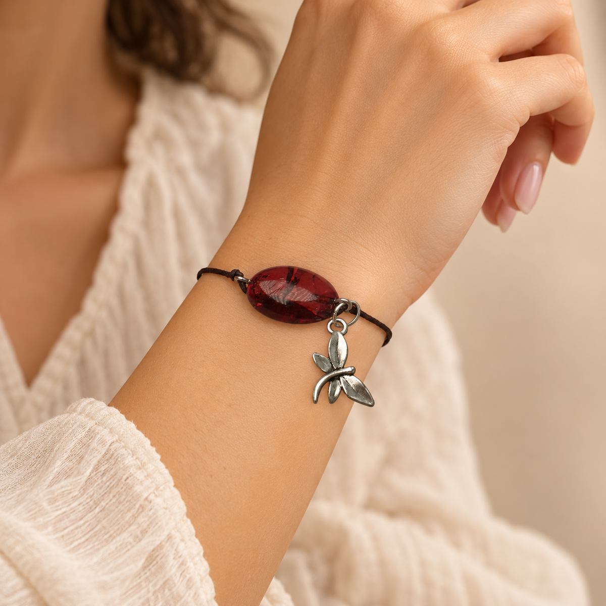 KIZIMA 3G0100q2.69 dark cherry oval amber cord bracelet with silver-tone dragonfly charm worn on an adult woman's wrist