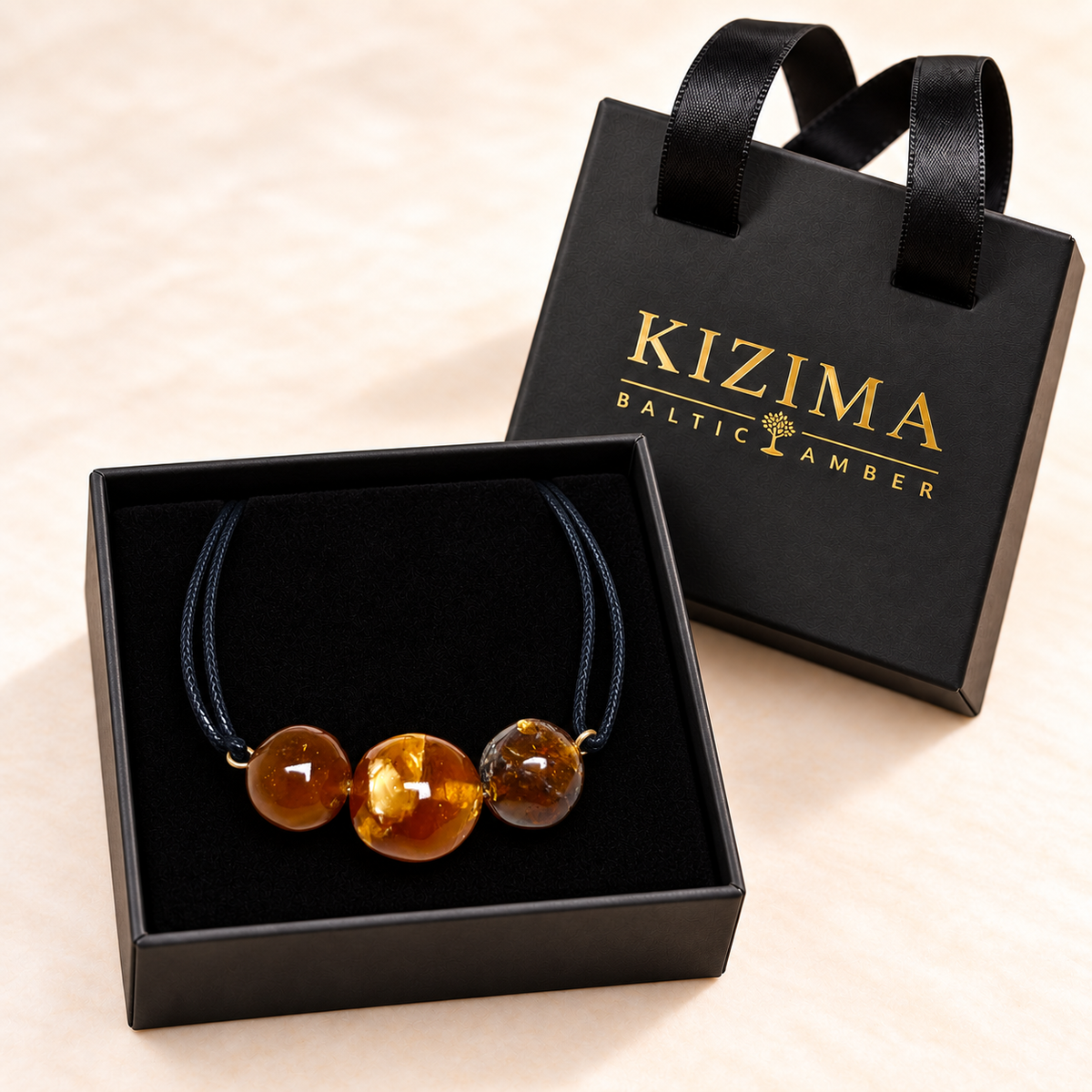 KIZIMA 3G0100q5.53 three-bead cognac and honey amber black-cord bracelet displayed on black velvet in the KIZIMA gift box