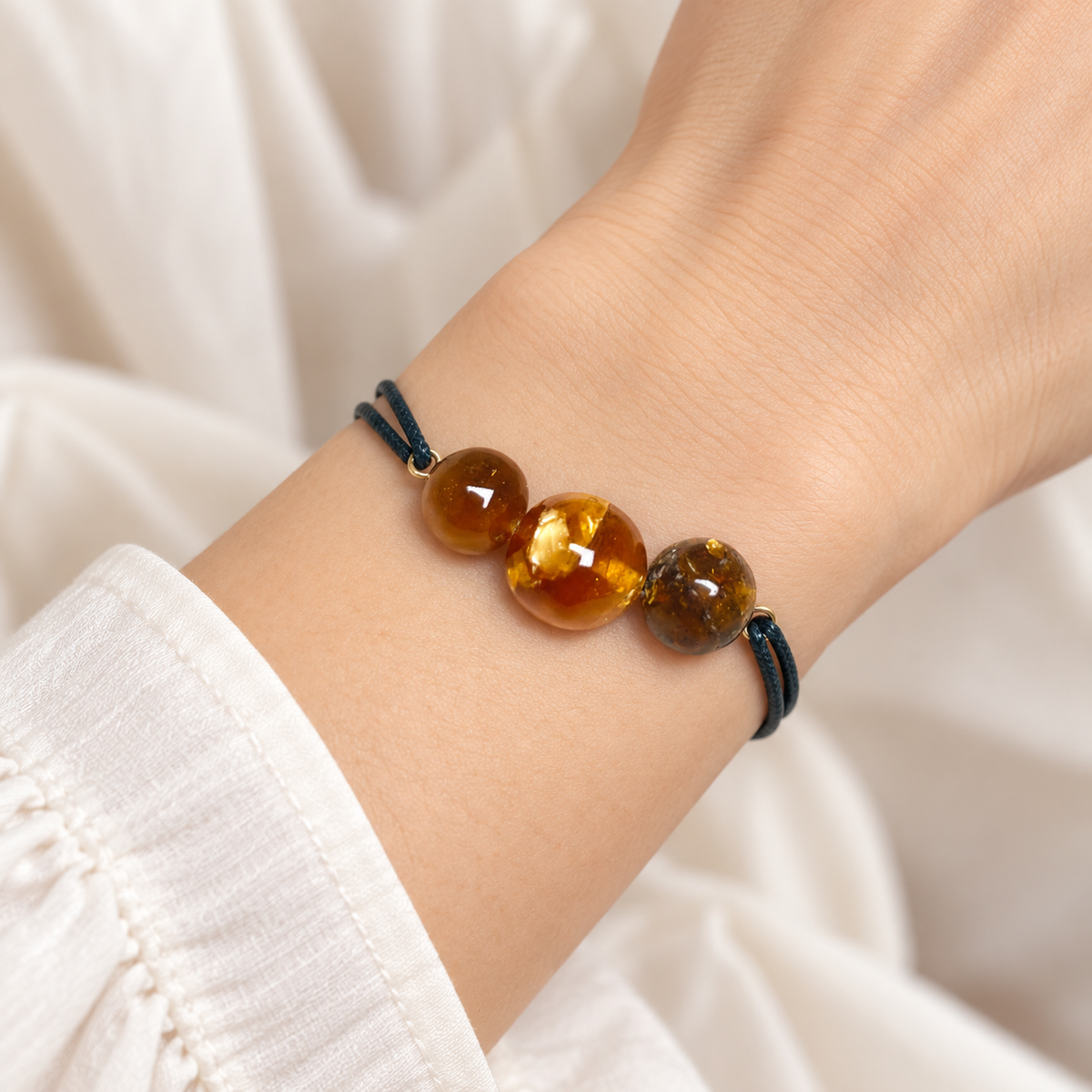 KIZIMA 3G0100q5.53 three amber bead bracelet with doubled black cord worn on an adult woman's wrist, front detail