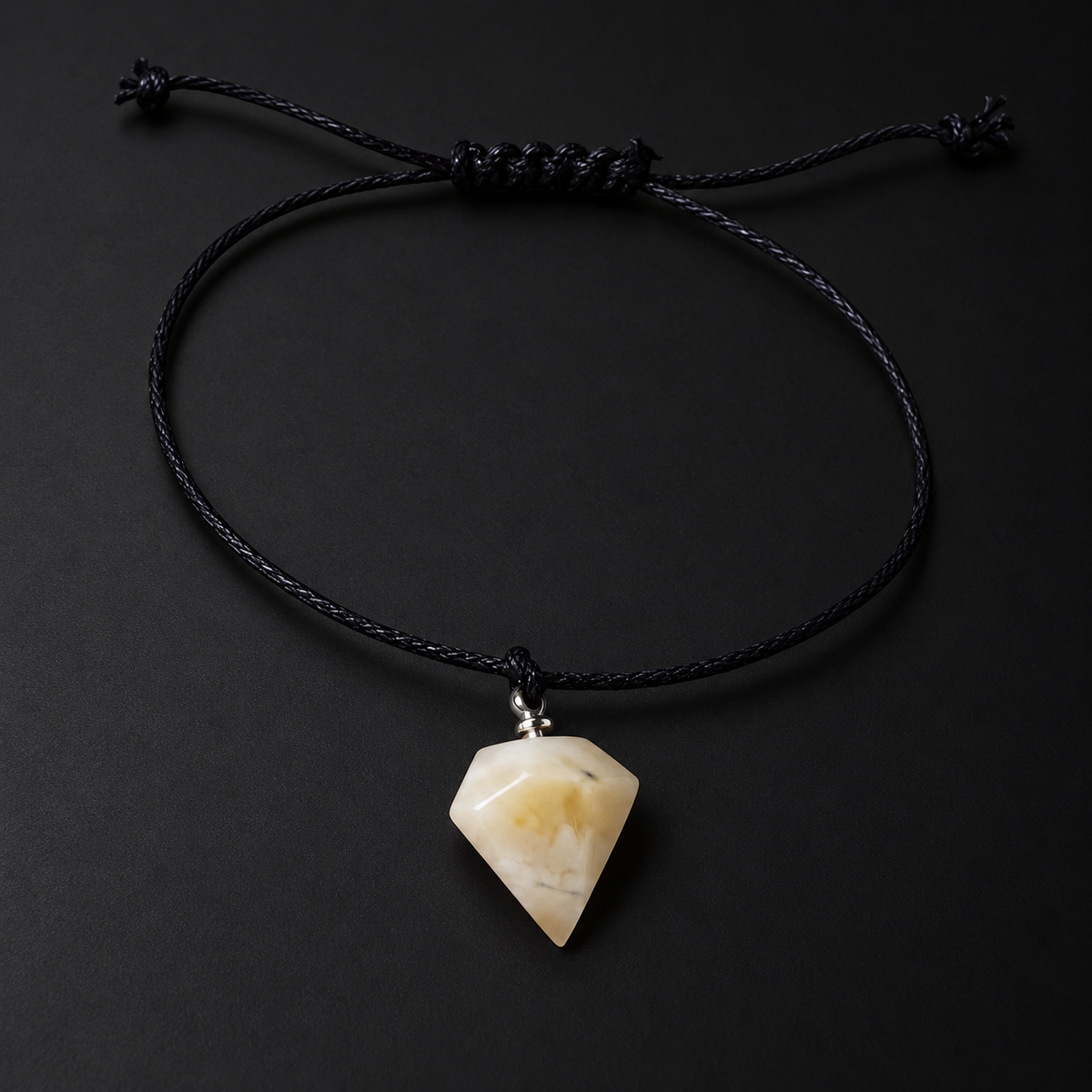 KIZIMA 3G0125q0.80 cream amber pointed pendant bracelet on black cord on a black studio background