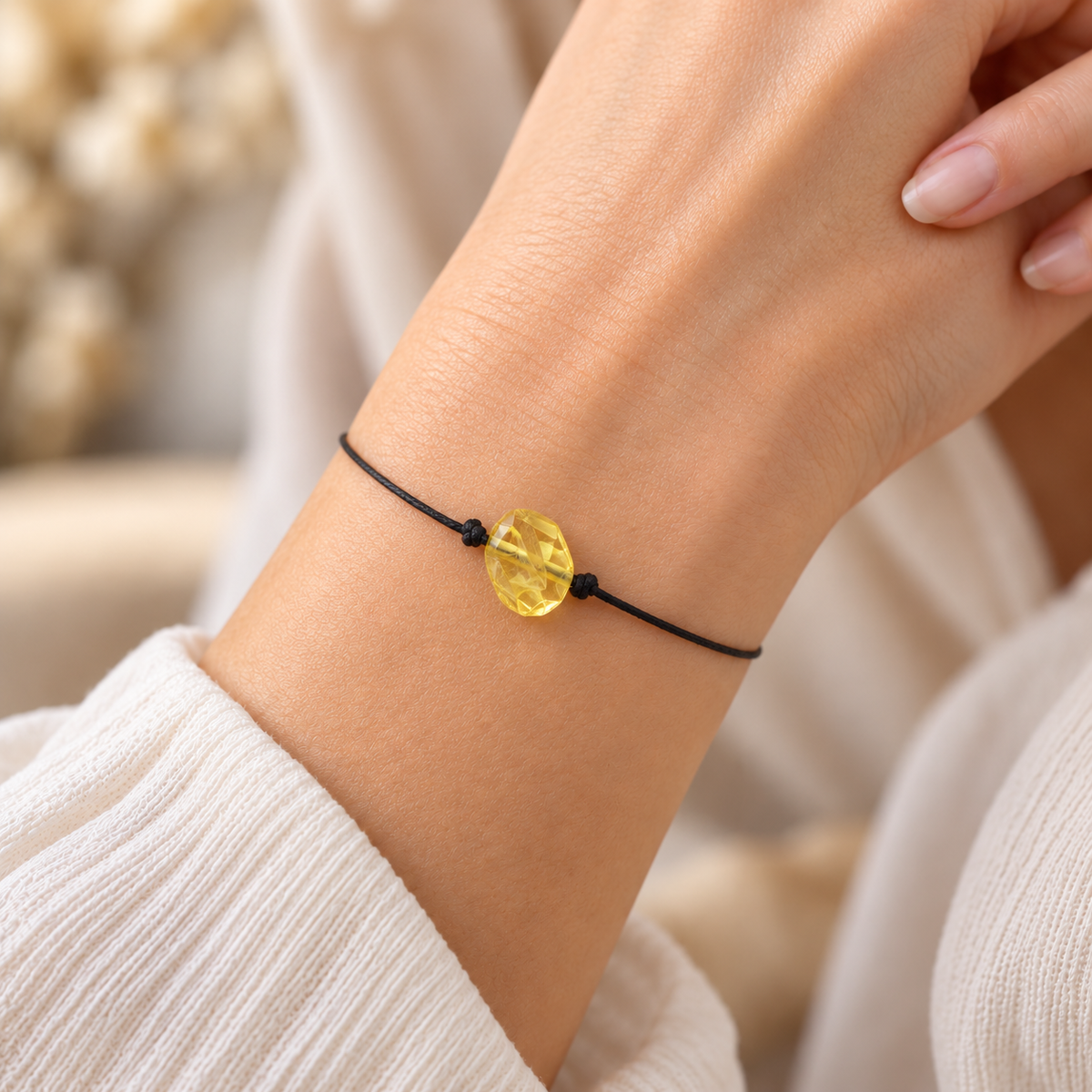 Minimalist pale yellow amber bracelet on a woman's wrist, with a single black cord and knotted sides
