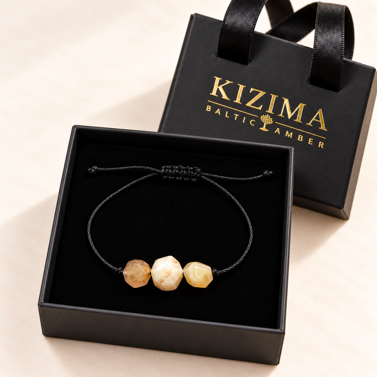 KIZIMA three faceted cream and peach amber stones on an adjustable black cord bracelet in a black KIZIMA gift box.