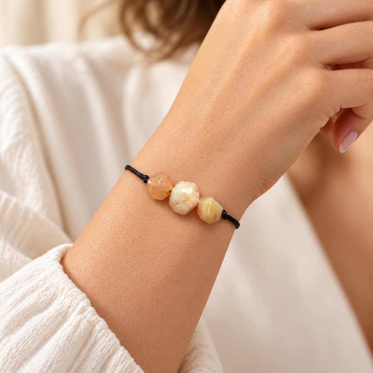 KIZIMA three faceted cream and peach amber stones on an adjustable black cord bracelet worn on a young adult woman's wrist.