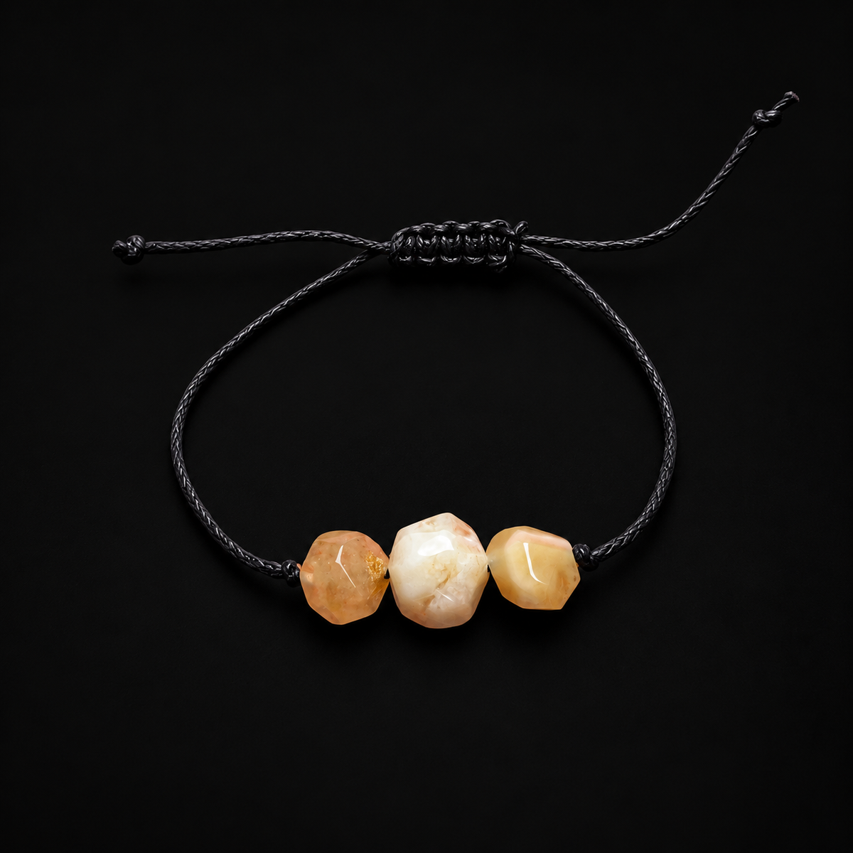 KIZIMA three faceted cream and peach amber stones on an adjustable black cord bracelet against black studio lighting.