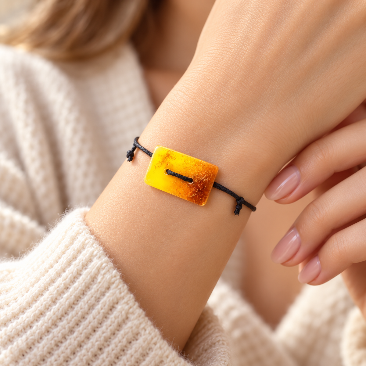 KIZIMA 3G0125q1.81 rectangular amber bracelet worn on a woman's wrist beside a cream knit cuff