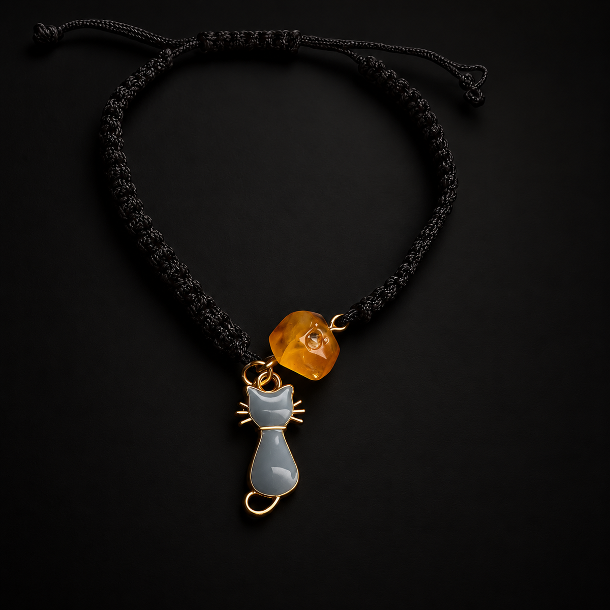 KIZIMA honey amber bead and gray cat charm black cord bracelet on a black studio background.