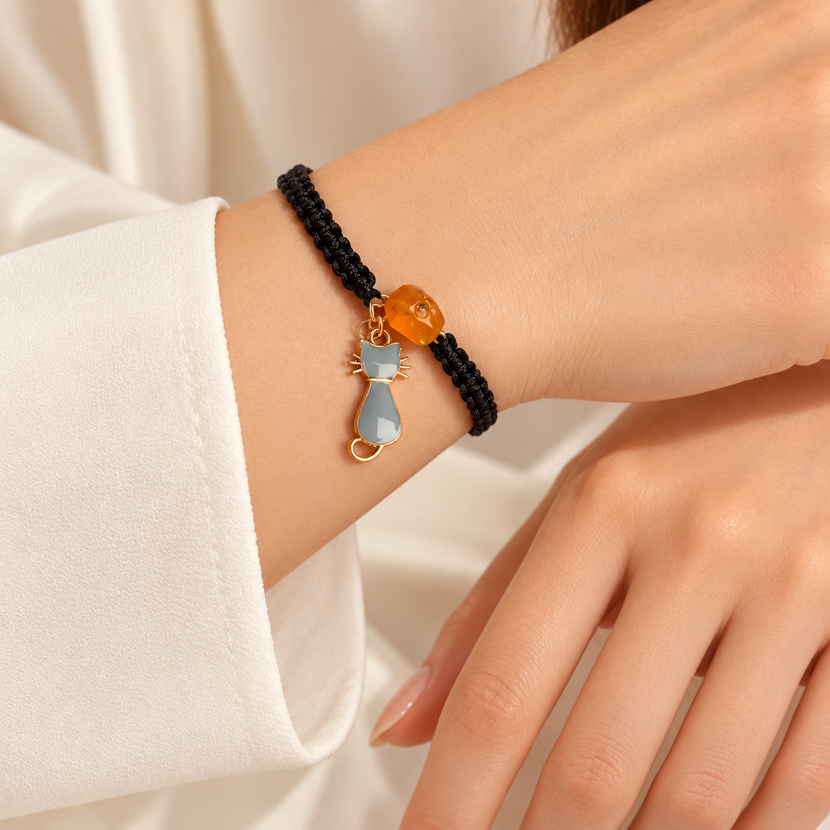 KIZIMA honey amber bead and gray cat charm black cord bracelet on a young adult woman's wrist.