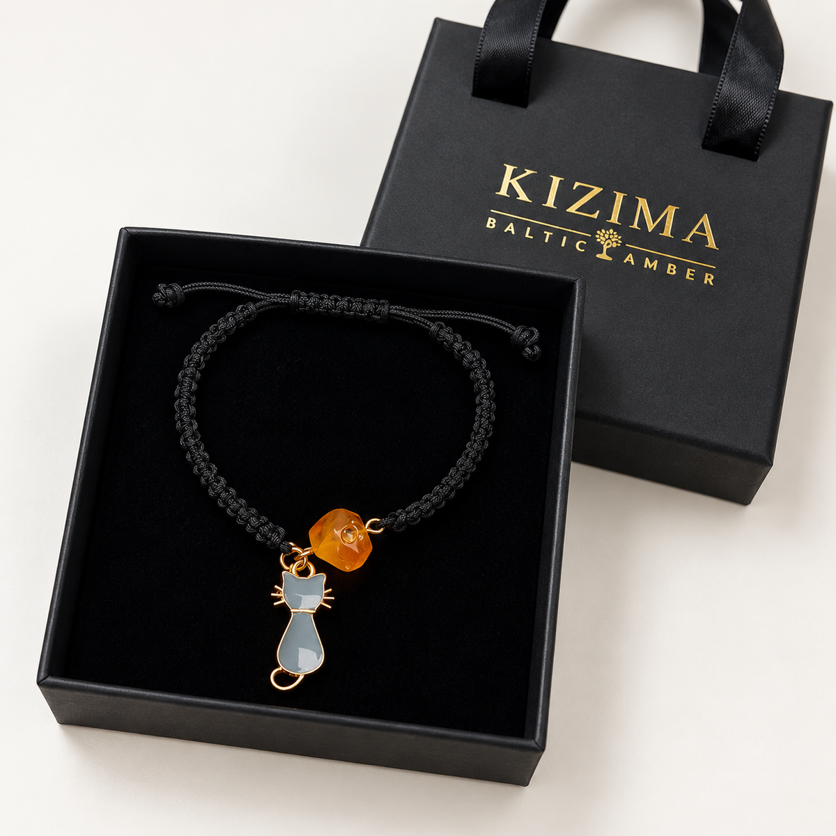KIZIMA honey amber bead and gray cat charm black cord bracelet in a KIZIMA gift box.