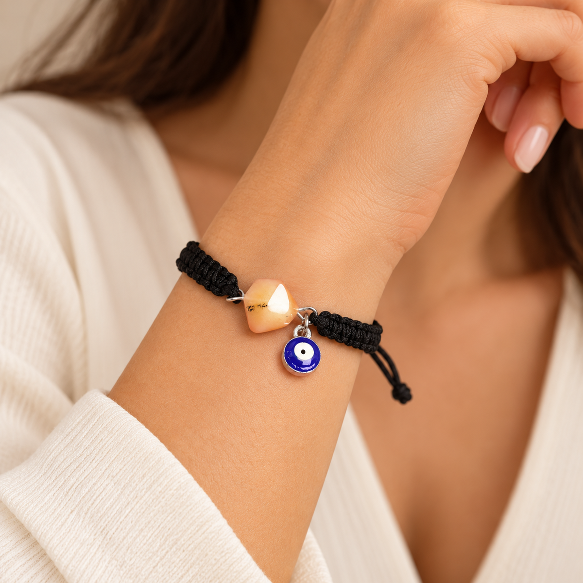 KIZIMA 3G0125q2.76-2 pale peach amber black macrame bracelet with blue evil-eye charm worn on an adult woman's wrist