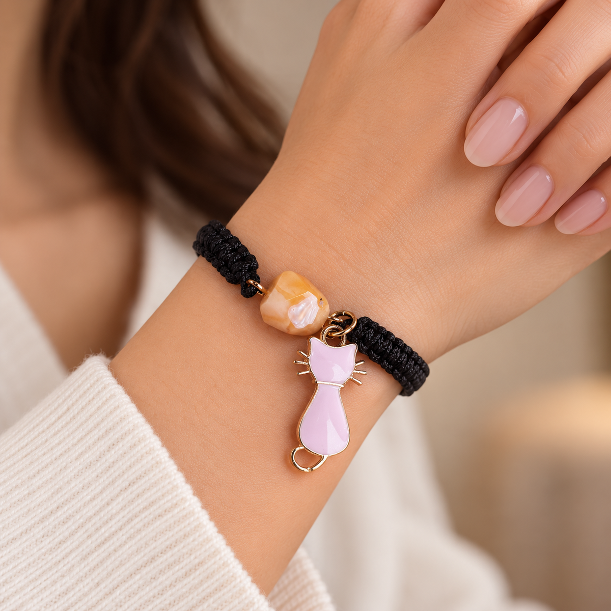 KIZIMA 3G0125q2.76-3 pale peach amber black macrame bracelet with pink cat charm worn on an adult woman’s wrist