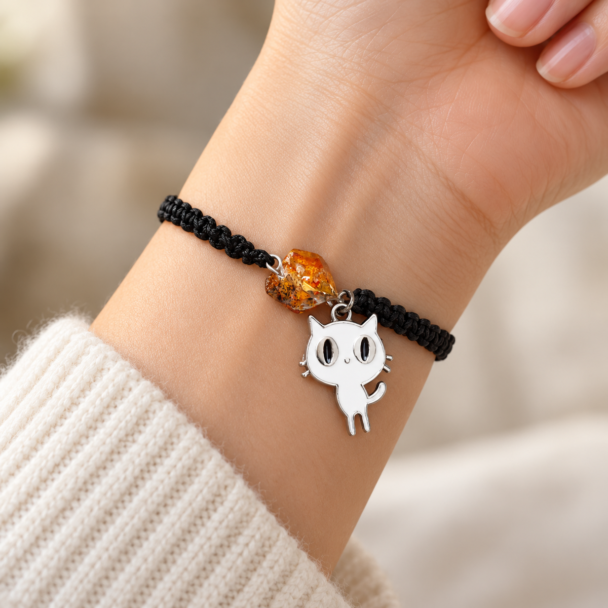 White cat charm and faceted honey amber bead on a black macrame bracelet worn on a woman's wrist