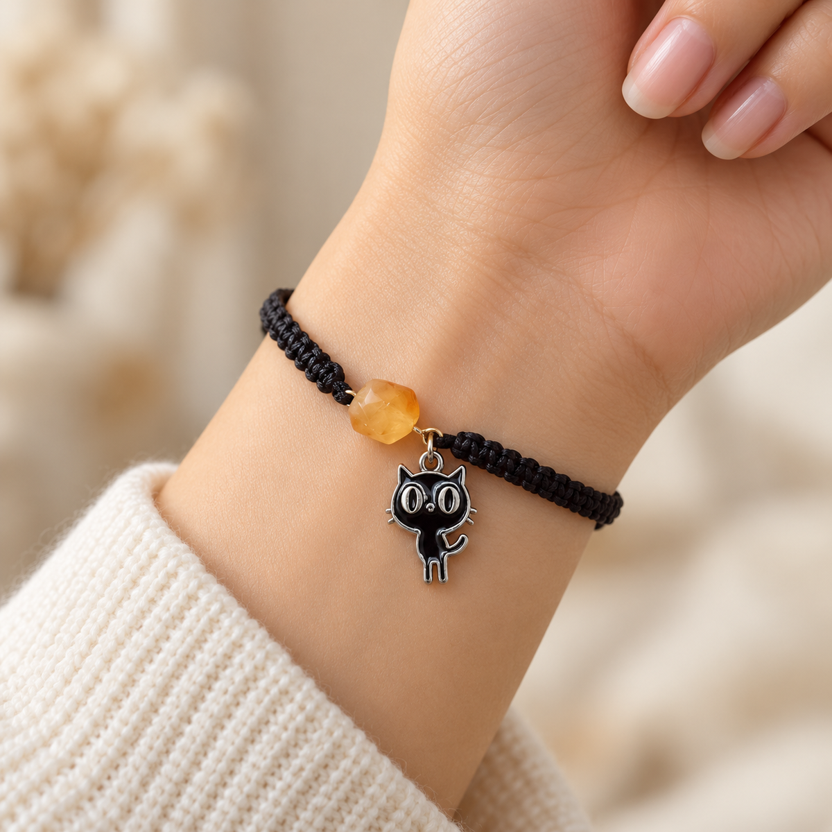 Black enamel cat charm and honey amber bead on a black adjustable bracelet around a woman's wrist