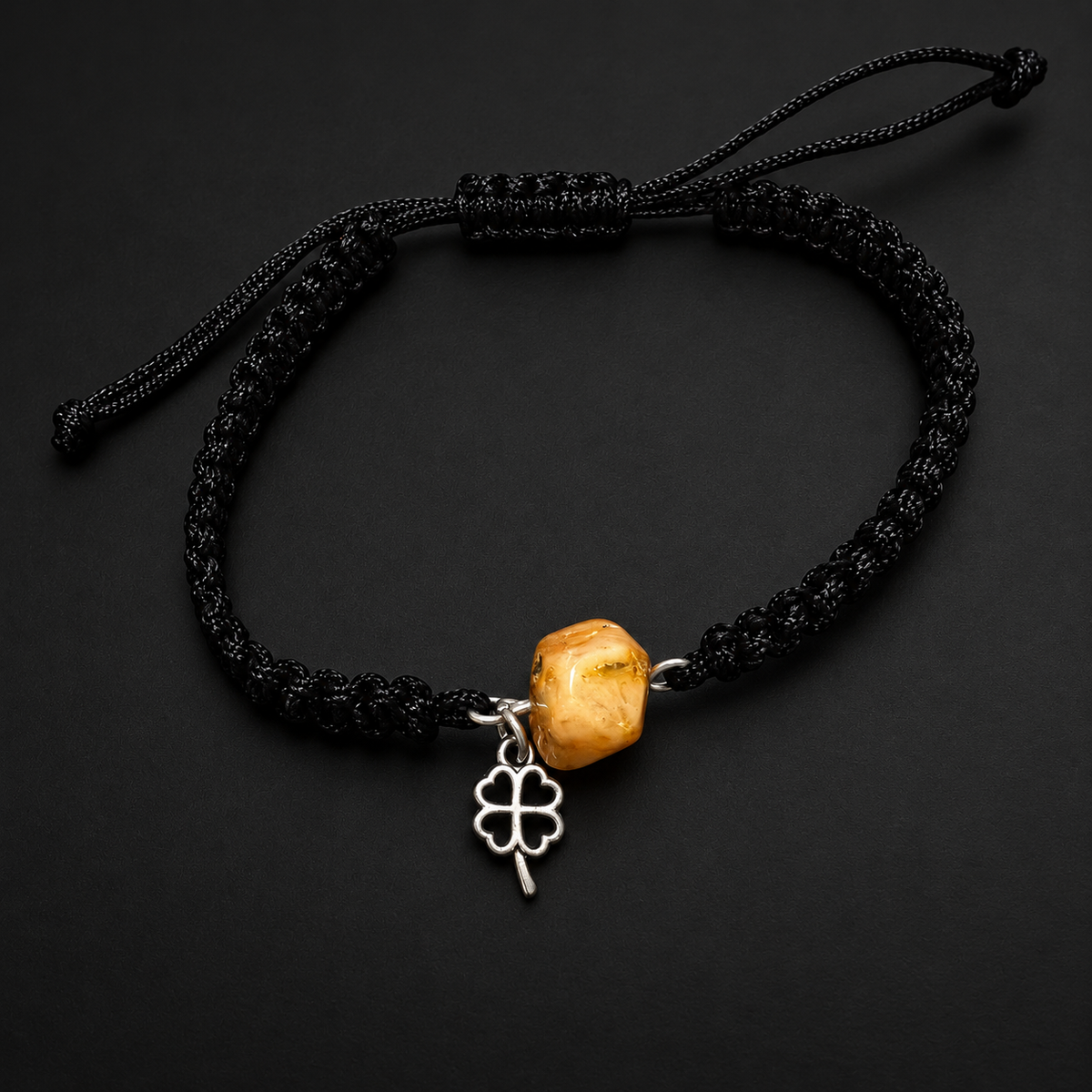 KIZIMA honey amber and open four-leaf clover charm bracelet with black macrame band in a dark studio