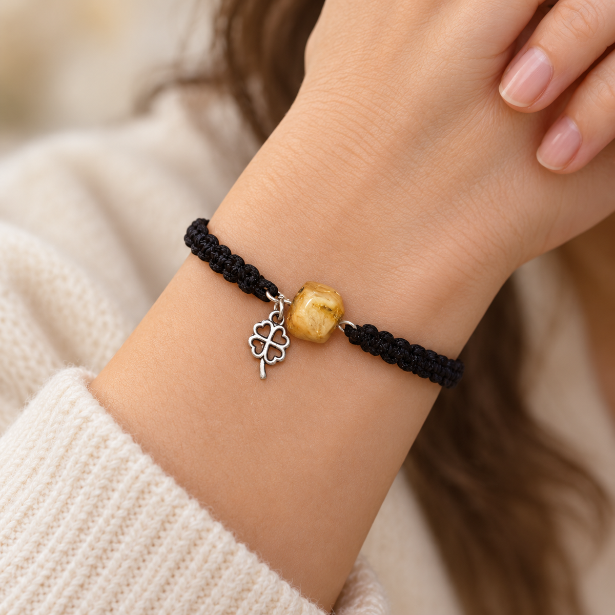 Honey amber bead and silver-tone clover charm on a black macrame bracelet worn around a woman's wrist