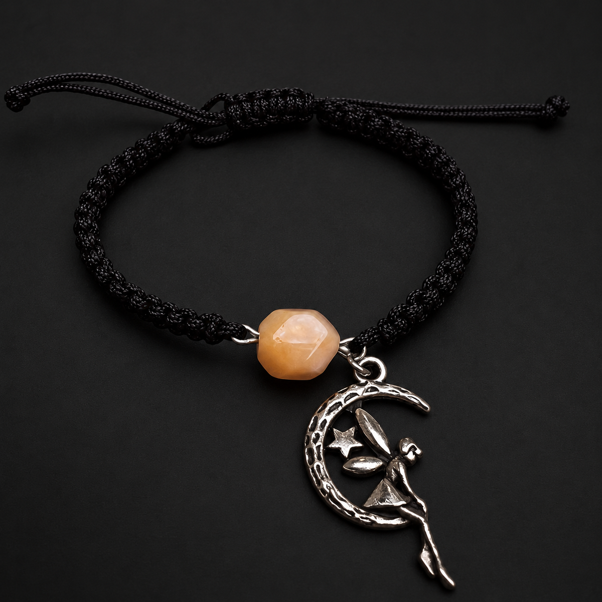 KIZIMA single creamy amber bead bracelet with a silver-tone moon and fairy charm on black macrame on a black studio background
