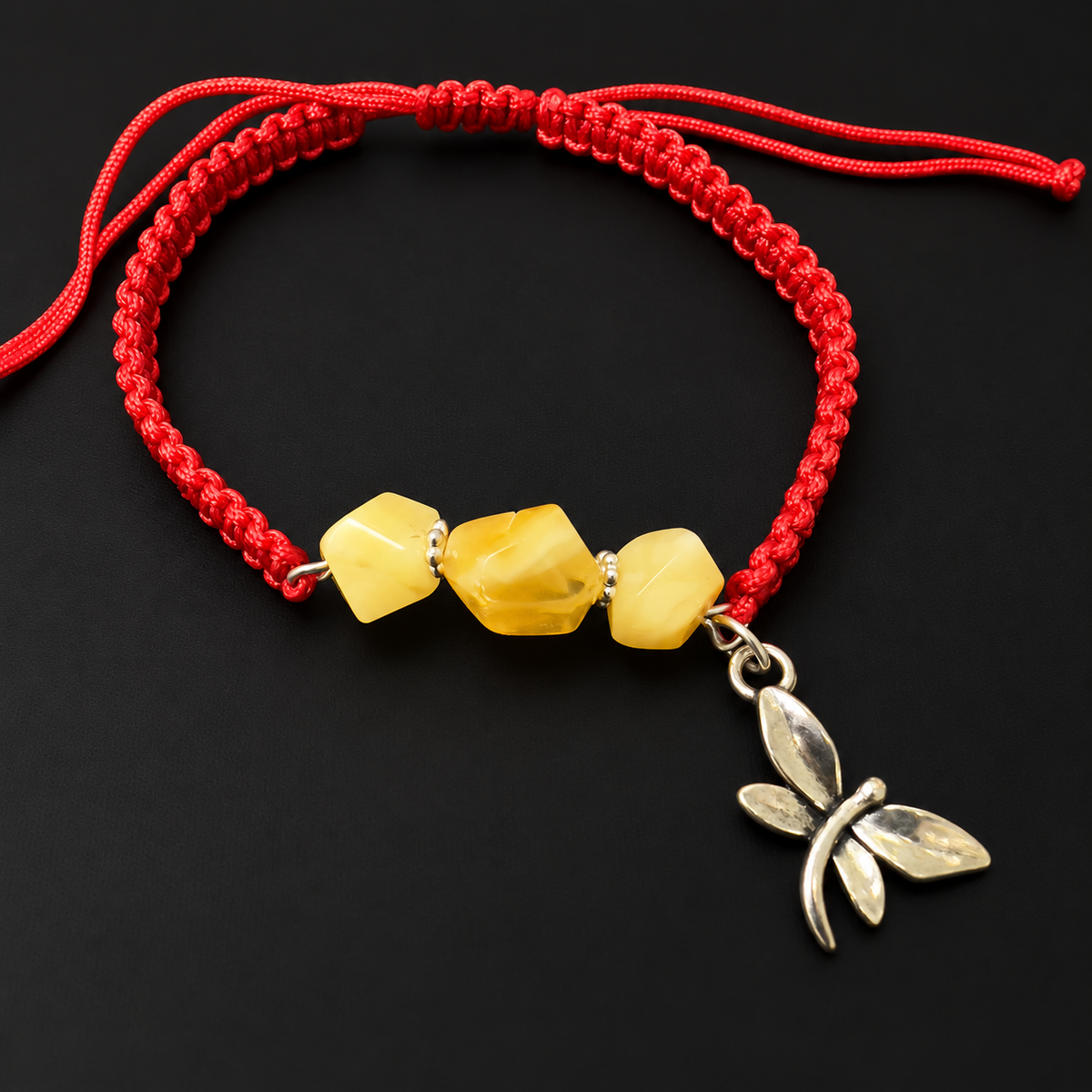 KIZIMA three yellow amber stones and silver-tone dragonfly charm on red macrame bracelet in a black studio