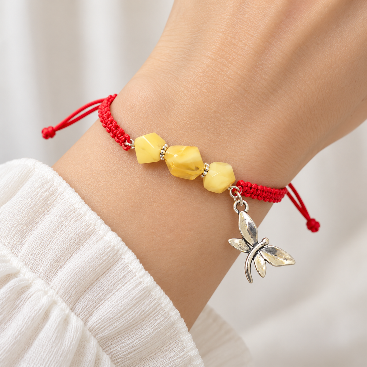 KIZIMA three yellow amber stones and silver-tone dragonfly charm on red macrame bracelet on a young adult woman's wrist