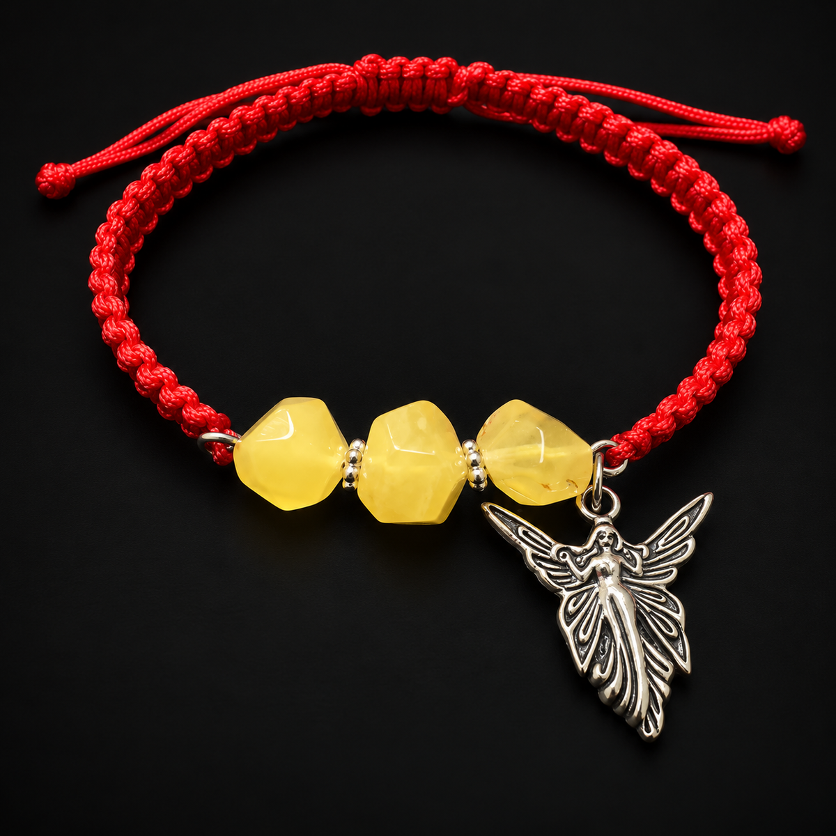 KIZIMA red macrame bracelet with three yellow amber stones and a silver-colored angel charm in black studio lighting.